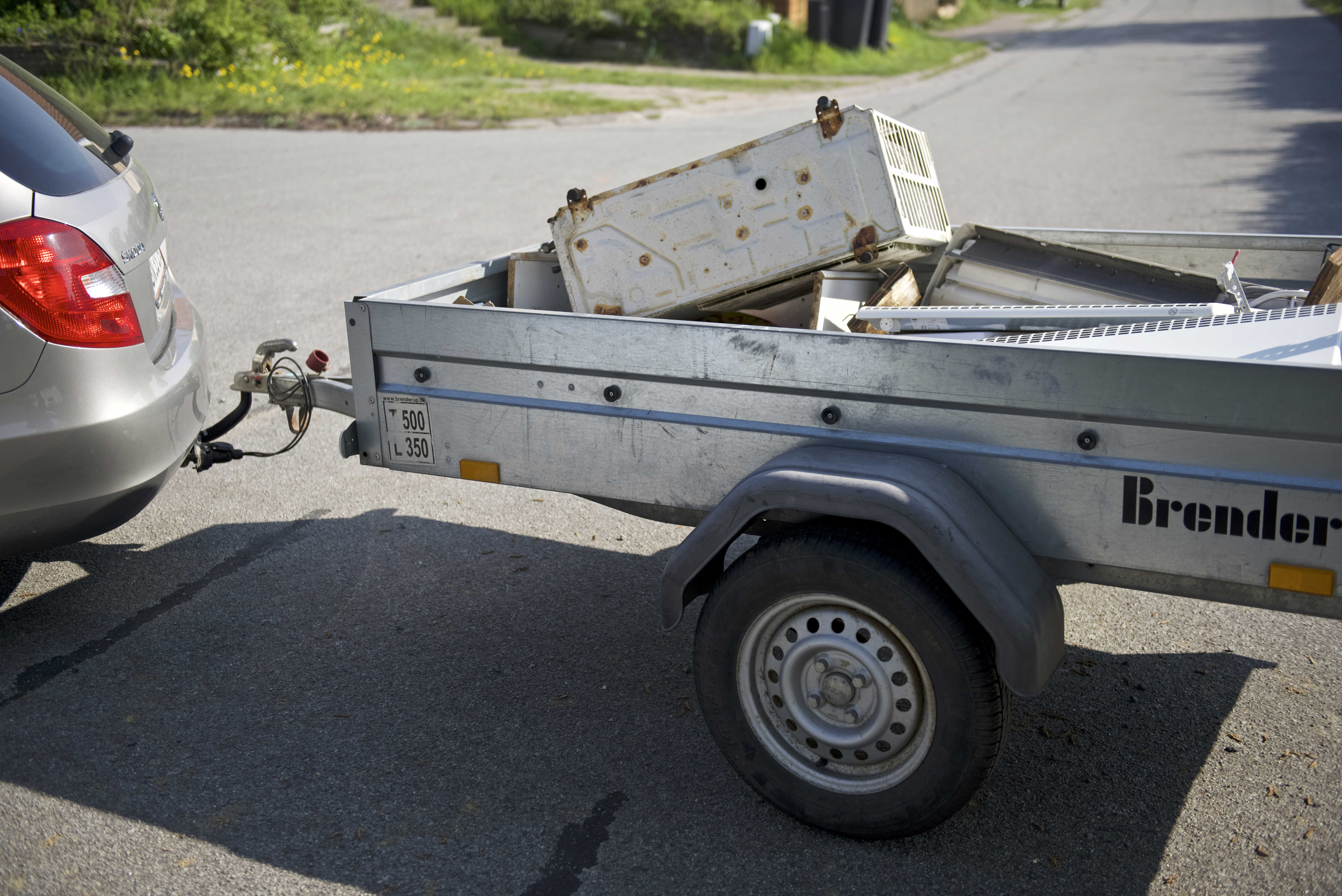 Trailer fyldt med gammelt elektronik og metaldele, tilkoblet en bil. Traileren er klar til at blive kørt til genbrugspladsen for korrekt affaldssortering og genbrug