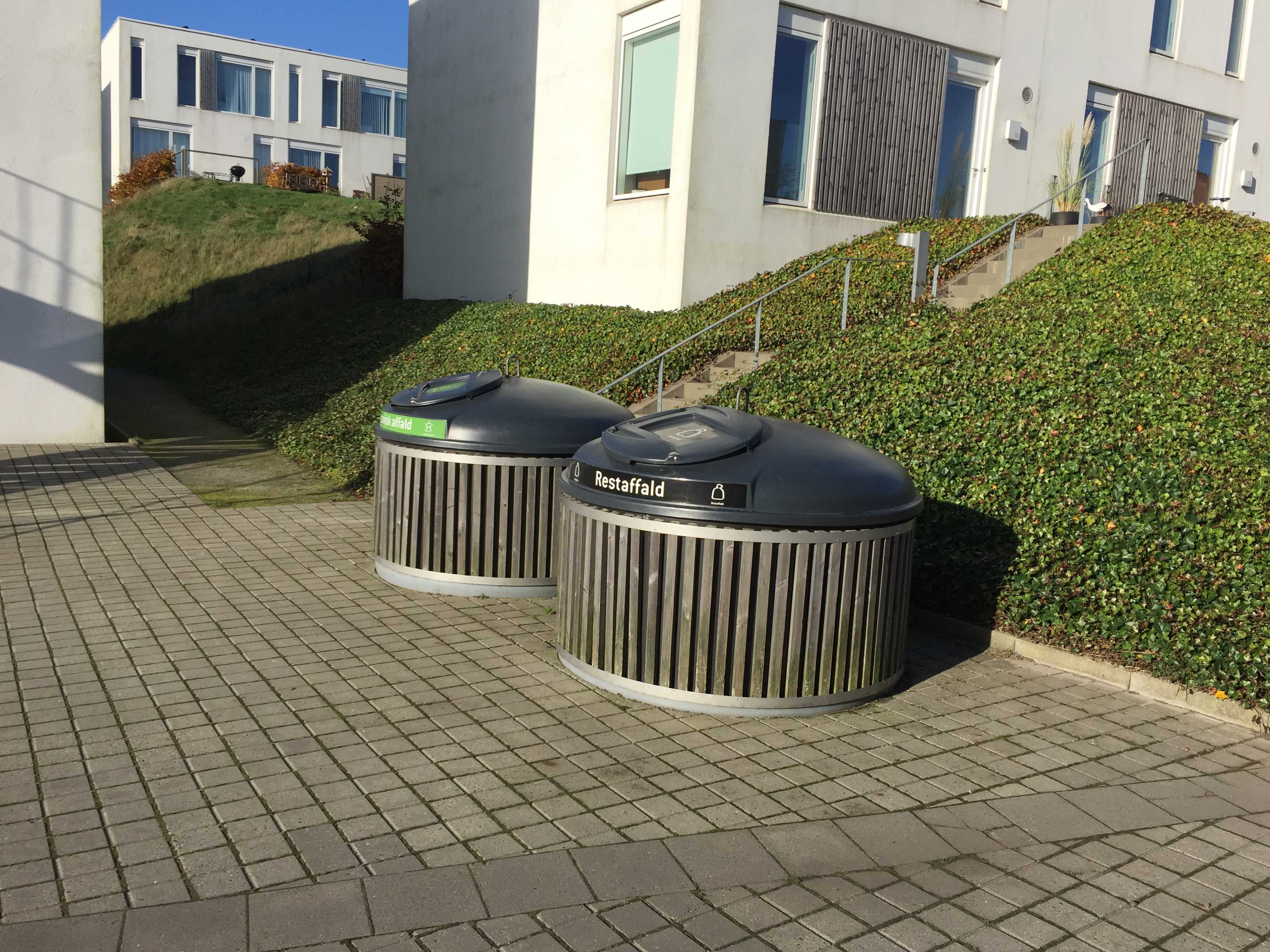 Rund nedgravet affaldsløsning nær i skrånende terræn ved moderne lejligheder