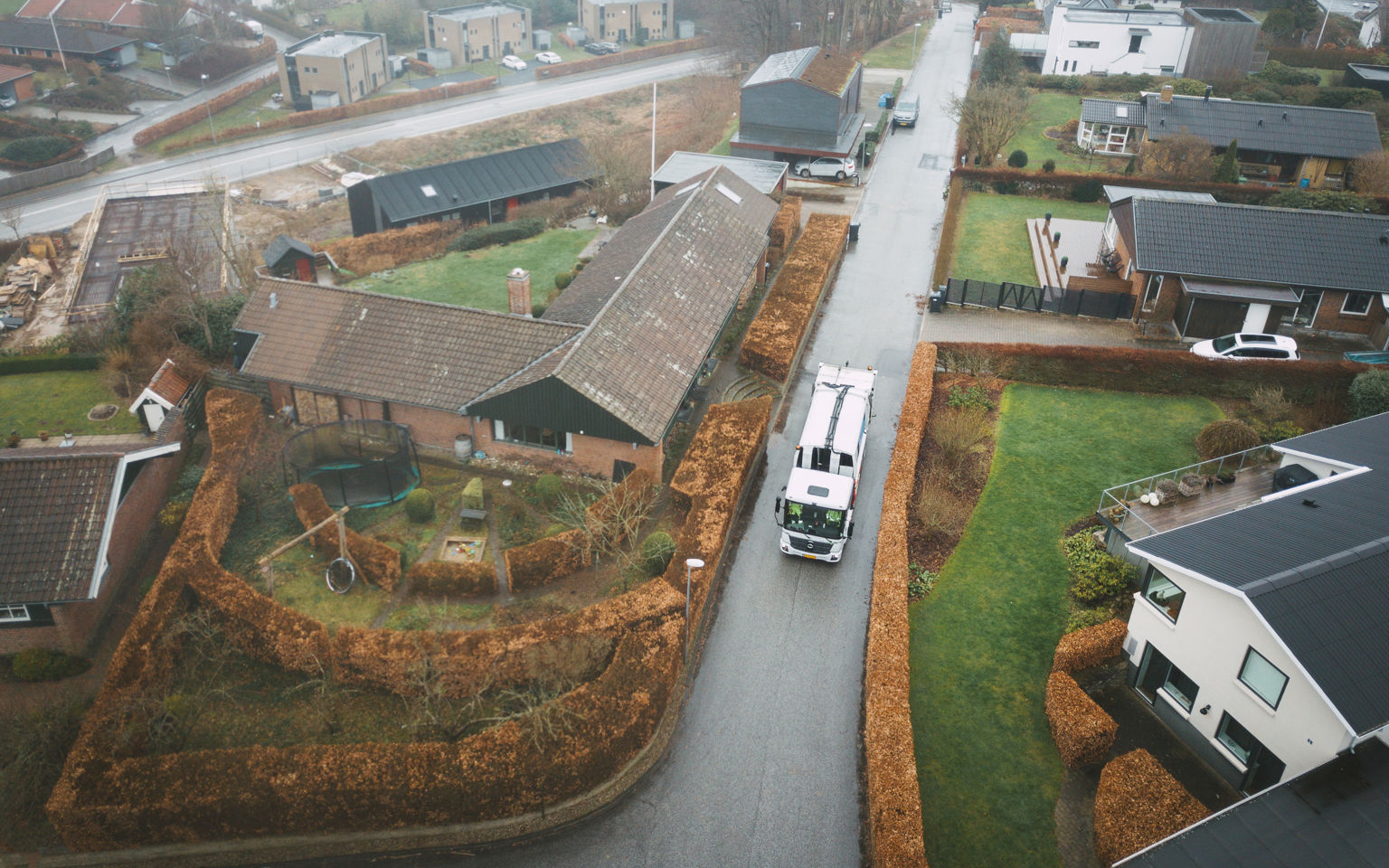 Oversigtsbillede af en affaldsindsamling i et villakvarter på en gråvejrsdag, med skraldebilen midt i arbejdet.