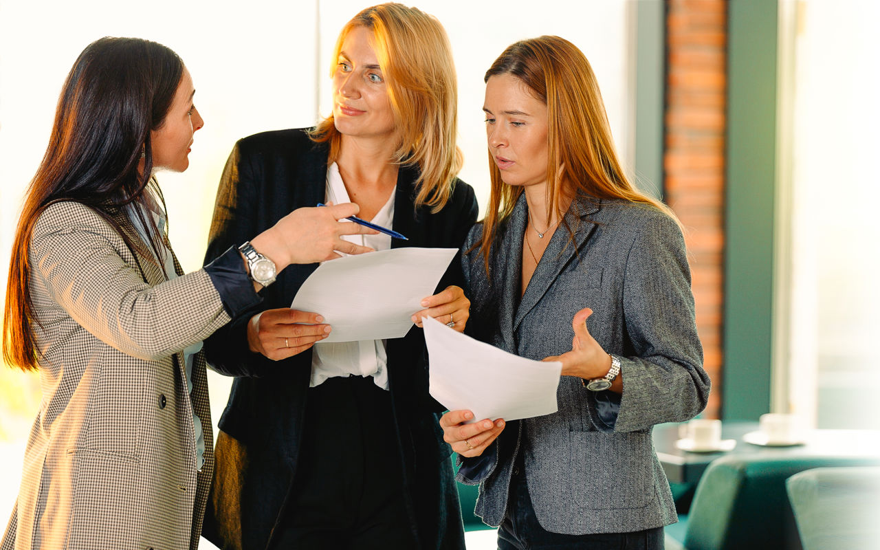 Foto af 3 kvinder stående i en samtalesituation